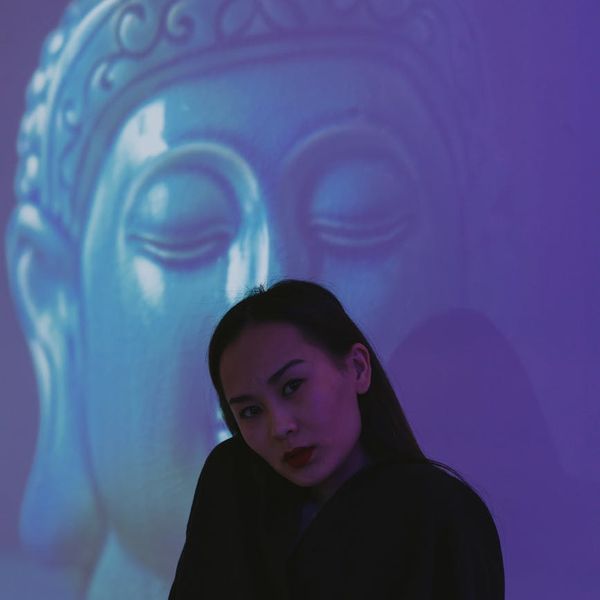 Woman in a calm yoga pose against a dark background with cyan light.